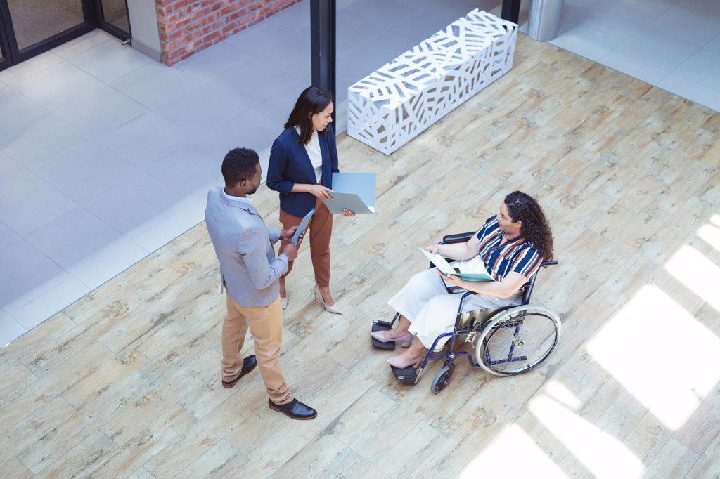 Two diverse business people talking with disabled female colleague in modern office. business and office workplace.