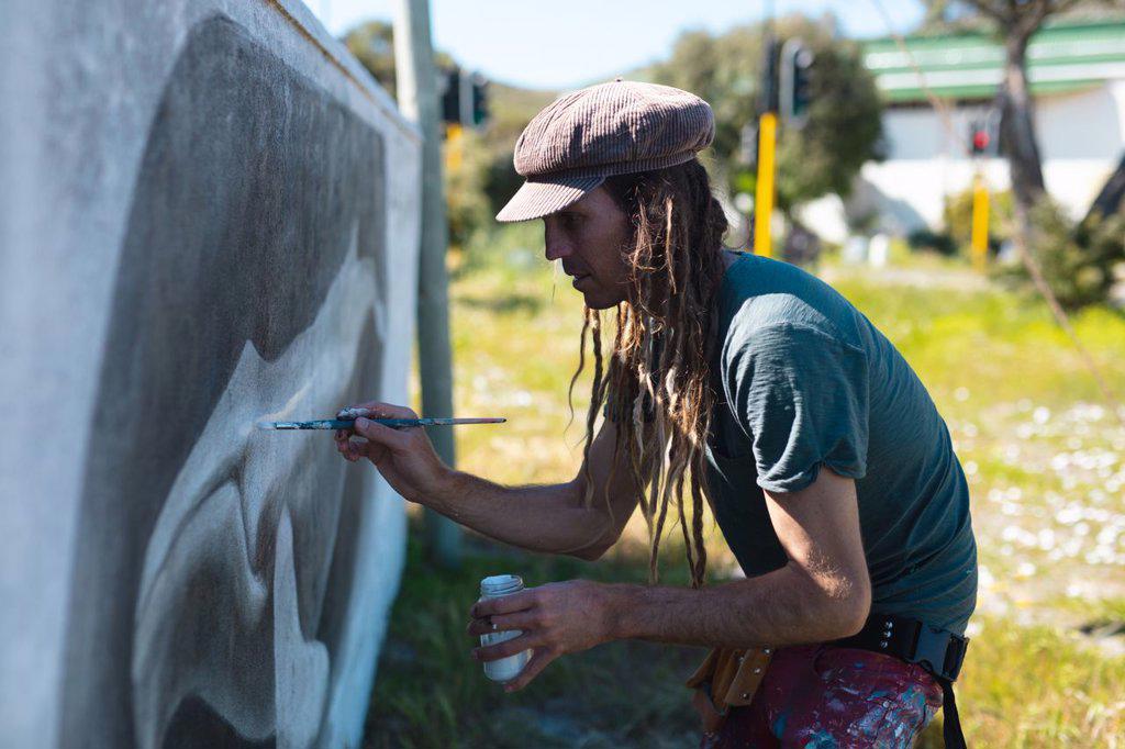 Male artist concentrating while making creative whale mural painting on wall with paintbrush. street art and skill.
