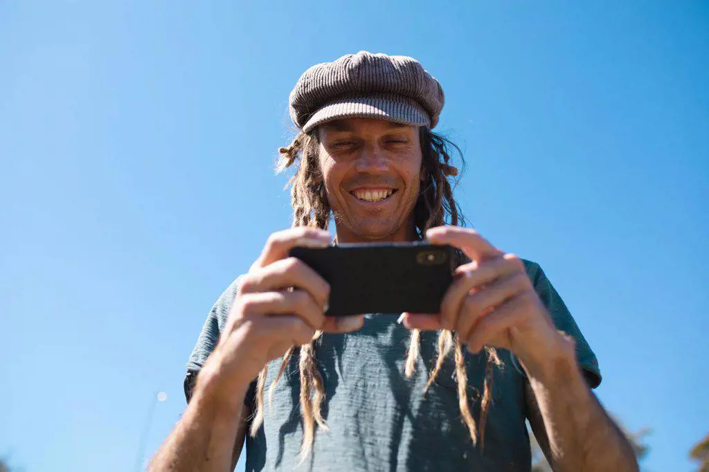 Smiling male hipster artist using smart phone against clear blue sky with copy space. technology and hipster people.