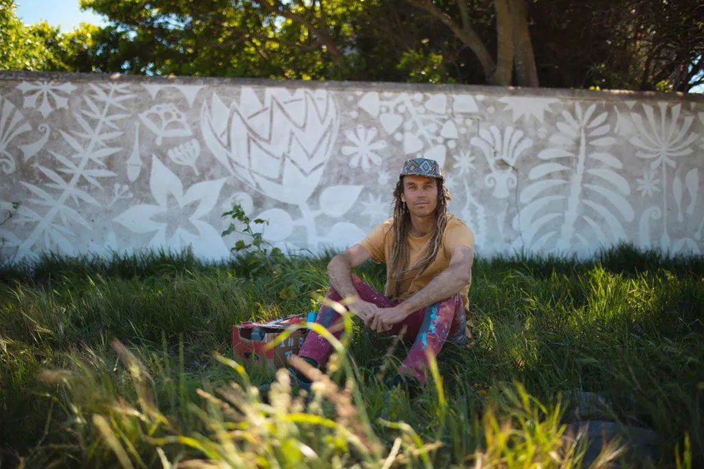 Portrait of male artist sitting on grass against abstract mural painting on wall. street art and skill.