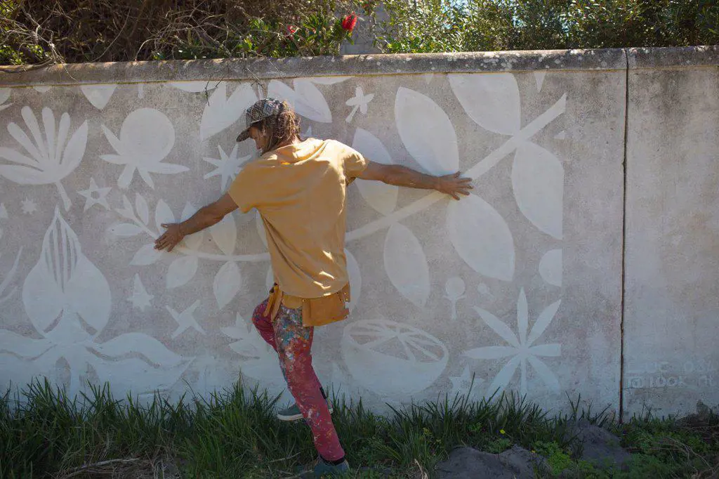 Rear view of male artist touching abstract mural painting on wall while walking on grass. street art and skill.