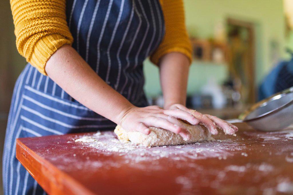 Midsection of woman wearing apron kneading dough on wooden table in kitchen at home. domestic lifestyle and healthy eating.