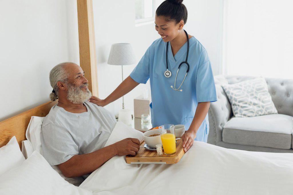 Side view of mixed race healthcare worker talking with old man in bed. Authentic Senior Retired Life Concept