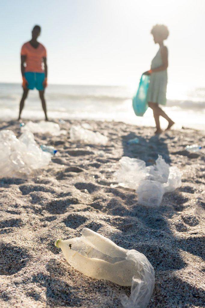 Surface level view of plastic garbage scattered against african american couple cleaning beach. unaltered, togetherness, responsibility and environmental issues concept.