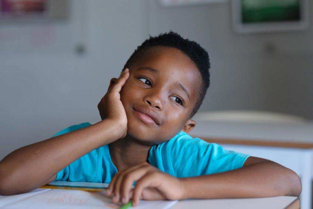 Close-up of african american elementary schoolboy looking away while leaning at desk in classroom. unaltered, education, childhood, contemplation, day dreaming and school concept.