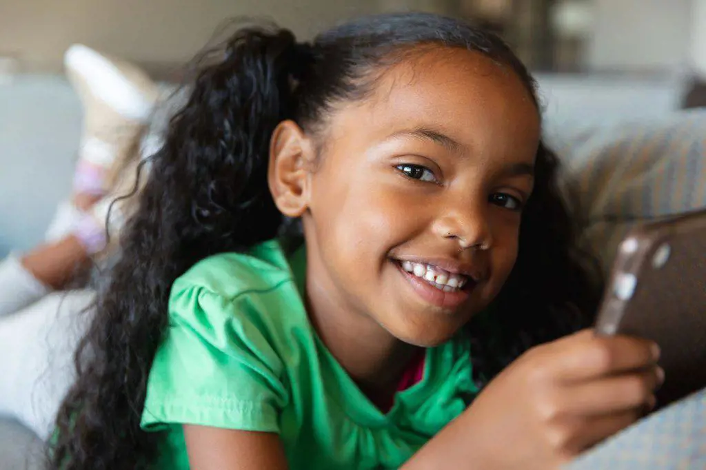 Portrait of smiling african american elementary girl using digital tablet while lying on couch. unaltered, education, childhood, relaxation, wireless technology, studying and school concept.