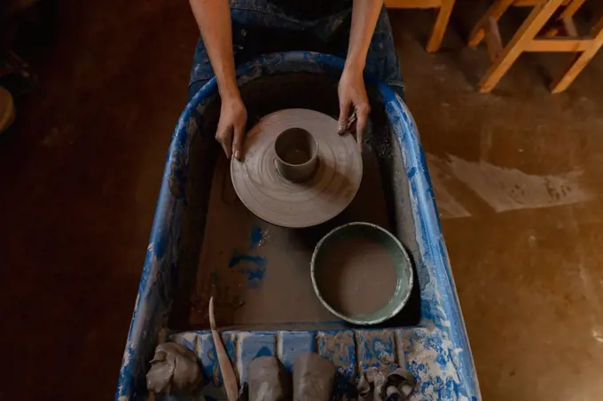 Elevated view of the hands of a young Caucasian female potter holding a potters wheel with a pot on it in a pottery studio