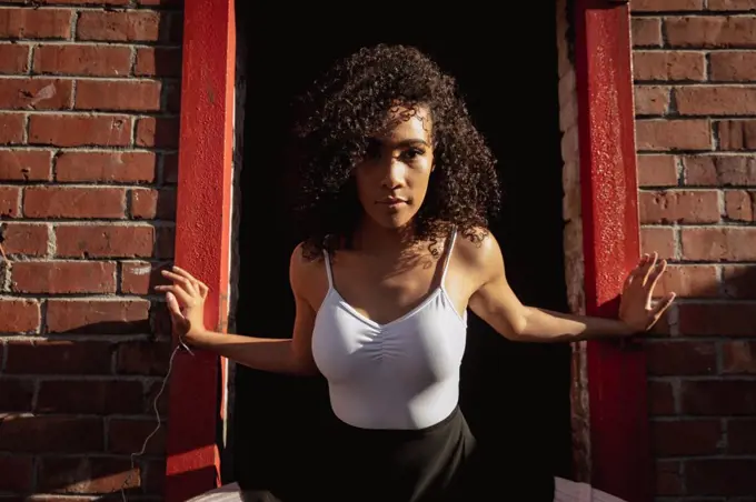 Front view close up of a young mixed race female ballet dancer standing in a doorway in a brick wall and looking straight to camera