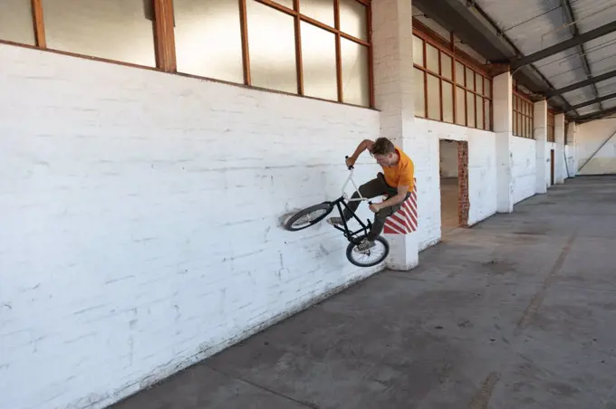 Front view of a young Caucasian man wallriding on a BMX bike in an abandoned warehouse