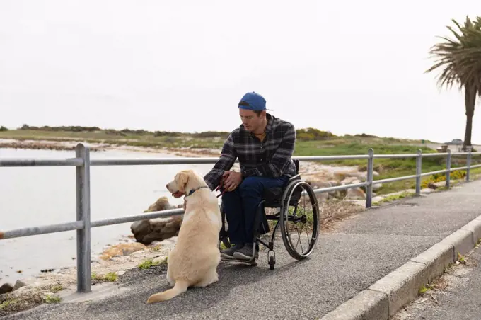 Front view of a young Caucasian man in a wheelchair taking a walk with his dog in the countryside by the sea