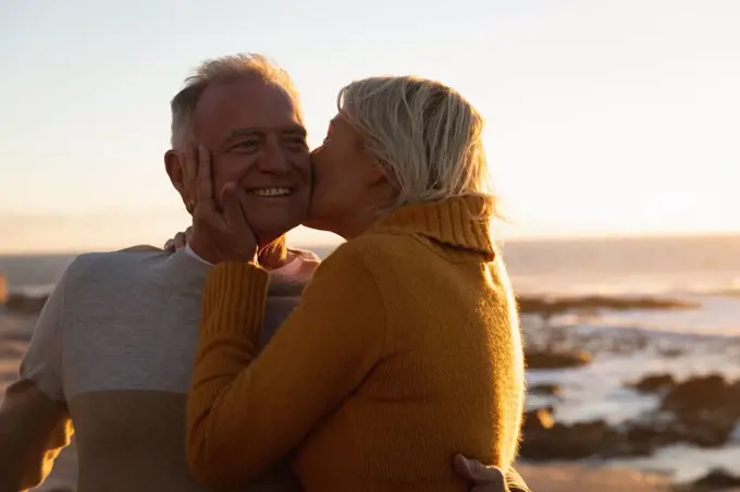 Side view close up of a mature Caucasian man and woman embracing and kissing by the sea at sunset