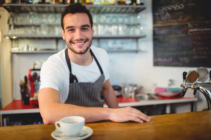Portrait of confident young waiter with coffee at counter in cafeteria