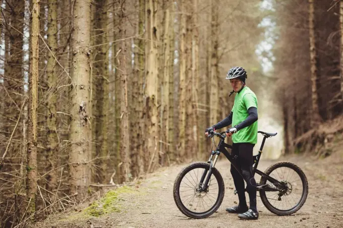 Side view of mountain biker standing by trees in forest