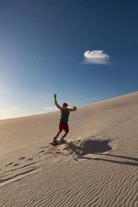 Man sandboarding on sand dune on a sunny day