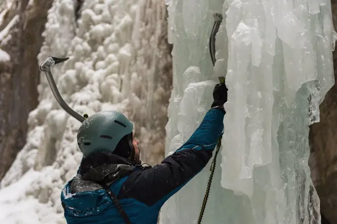 Male rock climber climbing ice mountain during winter
