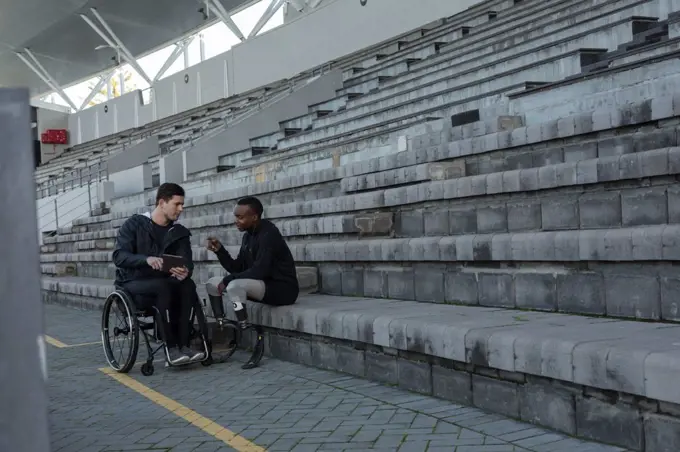 Two disabled athletics discussing over digital tablet at sports venue