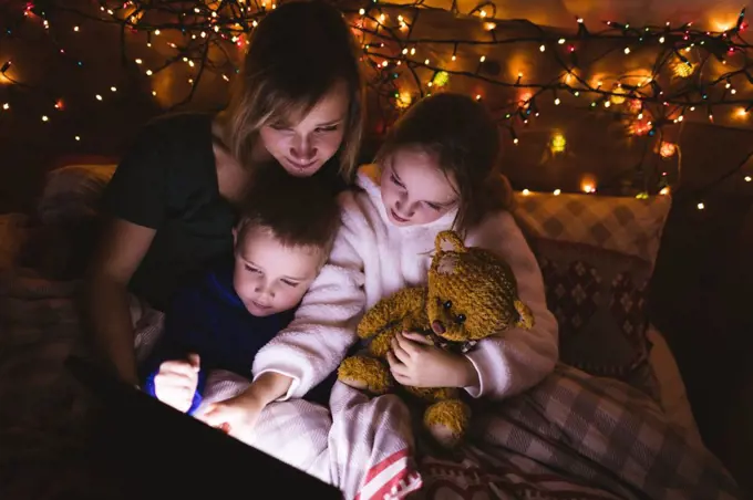 Mother and kids using digital tablet on bed against Christmas decoration