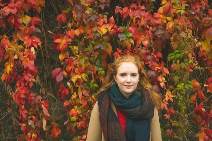 Redhead woman standing against plant creeper during autumn