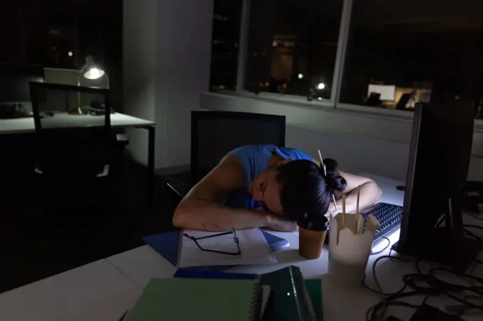 Front view of young mixed-race female executive sleeping at desk in a modern office