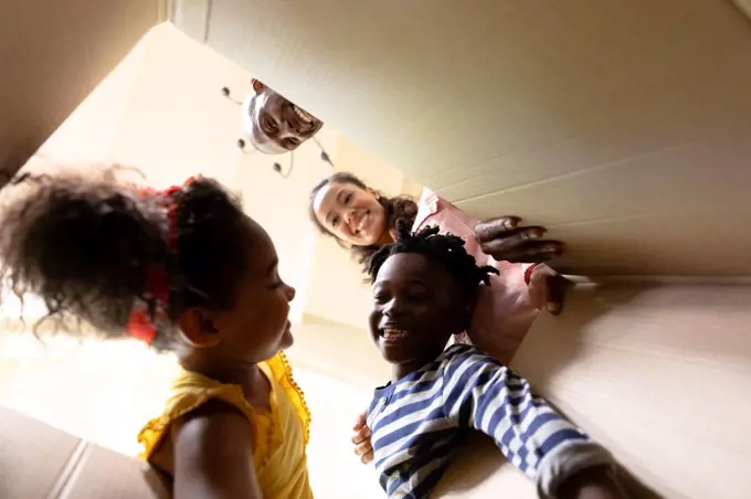 Low angle view of a mixed race couple and their young son and daughter looking at each other and reaching into a packing box they are opening in the hallway of their new home, and smiling