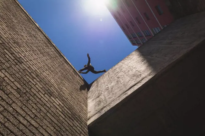 Side low angle view of a Caucasian man practicing parkour by the building in a city on a sunny day, jumping on the rooftop.