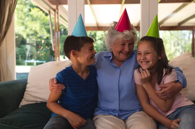 Senior caucasian woman spending time at home celebrating a birthday with her grandchildren, wearing party hats and smiling. quality time together in coronavirus covid 19 quarantine lockdown.