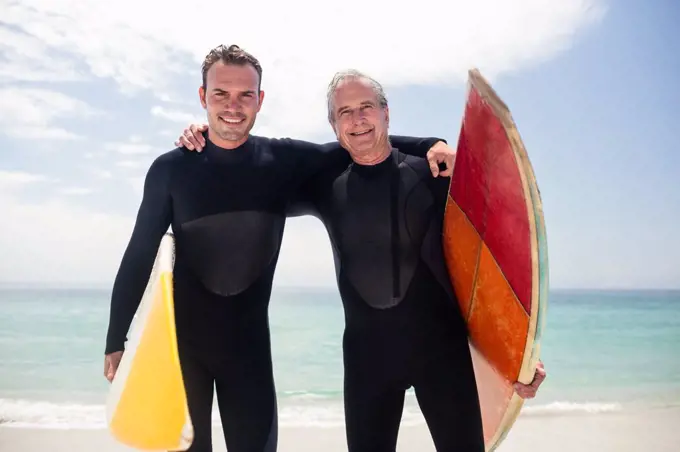 Portrait of happy father and son in wetsuit embracing on the beach on a sunny day