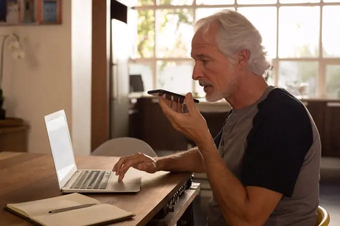Senior man talking on mobile phone while using laptop at home