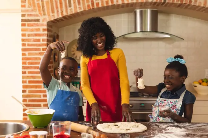 African american mother, son and daughter baking together and holding pieces of dough in the kitchen at home. christmas festivity tradition celebration concept