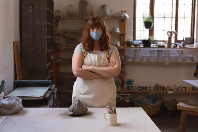 Portrait of caucasian woman wearing face mask at pottery studio. small creative business during covid 19 coronavirus pandemic.