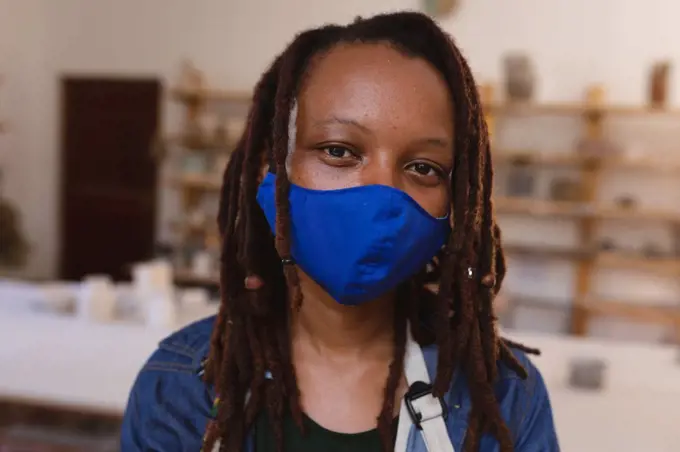 Portrait of mixed race woman wearing face mask at pottery studio. small creative business during covid 19 coronavirus pandemic.