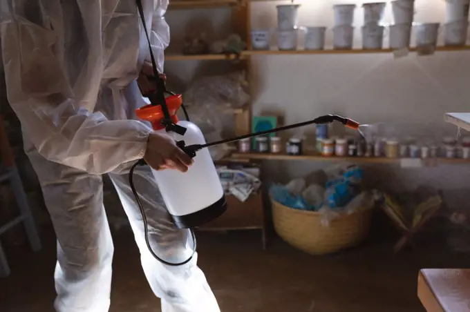Caucasian male cleaner in protective clothes working in pottery studio. disinfecting the whole place. small creative business during covid 19 coronavirus pandemic.