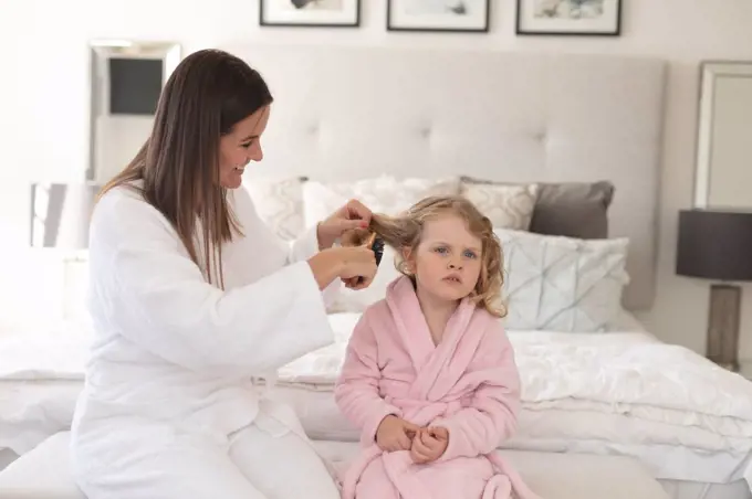 Caucasian woman and daughter having fun in bedroom. mother is brushing daughter hair. enjoying quality time at home during coronavirus covid 19 pandemic lockdown.