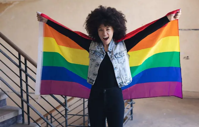Mixed race woman holding rainbow flag shouting to camera. gender fluid lgbt identity racial equality concept.