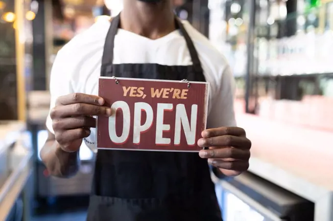 Portrait of african american male barista holding a were open card. independent small business owner.
