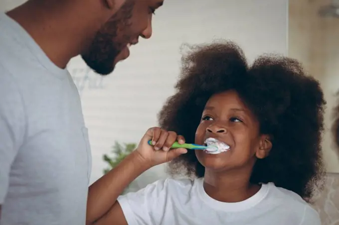 African american girl and her father brushing teeth together. staying at home in self isolation during quarantine lockdown.