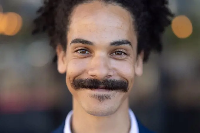Portrait of mixed race male with moustache looking to camera and smiling. independent small business in a city.