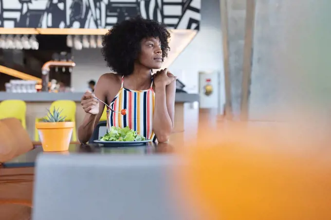 African american woman sitting at table and eating in restaurant. independent cafe, small successful business.