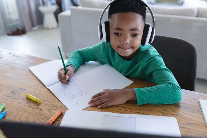 African american boy in online school class, using headphones and laptop. at home in isolation during quarantine lockdown.