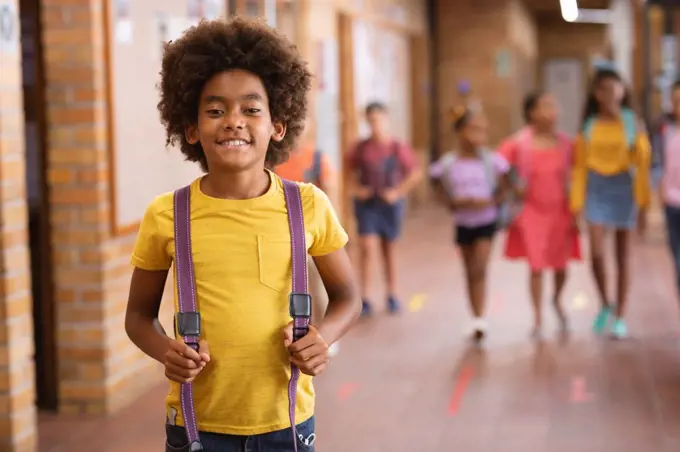 Portrait of african american boy smiling while standing in the corridor at school. school and education concept