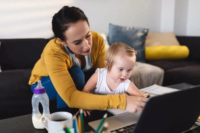 Caucasian mother holding her baby using laptop while working from home. motherhood, love and baby care concept