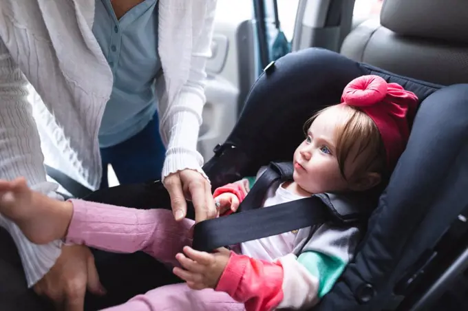Mid section of mother putting her baby in safety baby seat in the car. motherhood, love and baby care concept