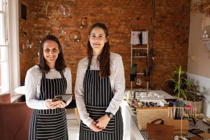 Caucasian business owner and waitress wearing aprons, looking at camera, smiling. small independent cafe business.