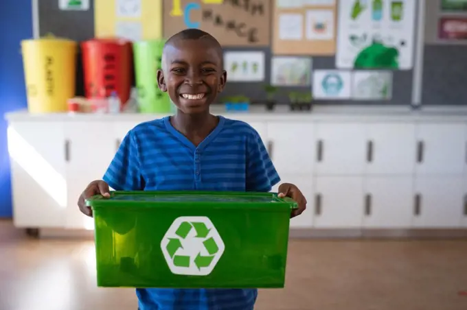Portrait of african american boy holding tray filled with recyclable plastic items at school. school and education concept