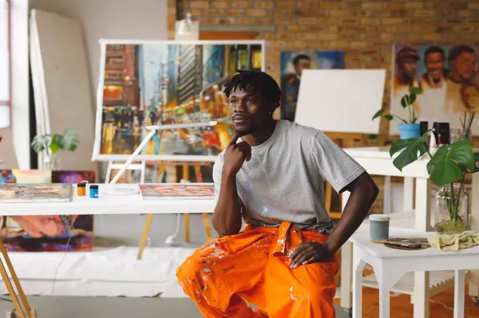 African american male painter at work sitting and thinking in art studio. creation and inspiration at an artists painting studio.