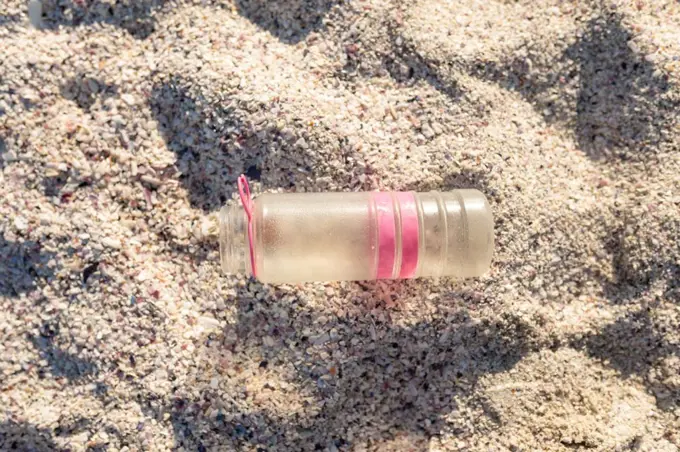 Directly above view of abandoned plastic bottle on white sand at beach during sunny day. unaltered, environmental damage and plastic pollution concept.