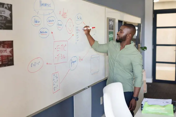 African american young male teacher writing on whiteboard while teaching in classroom. unaltered, education, teaching, occupation and school concept.