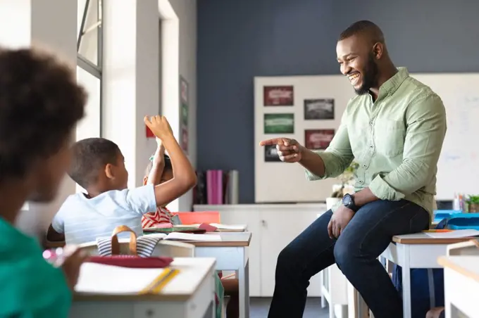Smiling african american young male teacher gesturing on african american elementary boy at desk. unaltered, education, learning, childhood, teaching, occupation and school concept.