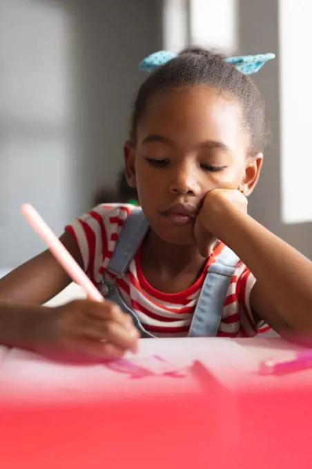 Close-up of african american elementary schoolgirl drawing on book at desk in classroom. unaltered, education, learning, art, childhood, studying and school concept.