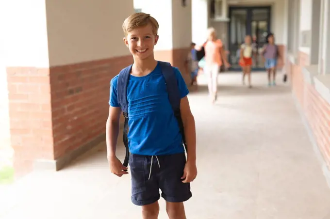 Portrait of smiling caucasian elementary schoolboy standing in corridor. unaltered, education, childhood and school concept.